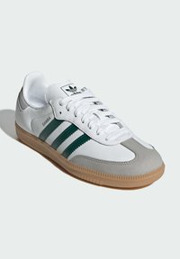 Bijele kožne tenisice s akcentima od sive suede, zelenim prugama i gumiranim potplatom. Pertle i Adidas logo na jeziku.