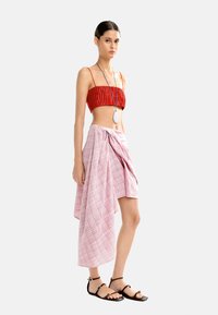 Czerwony plisowany top typu crop zestawiony z różowo-białą spódnicą w kratkę. Modelka ma na sobie czarne sandały na cienkich paskach i srebrny naszyjnik z zawieszką.