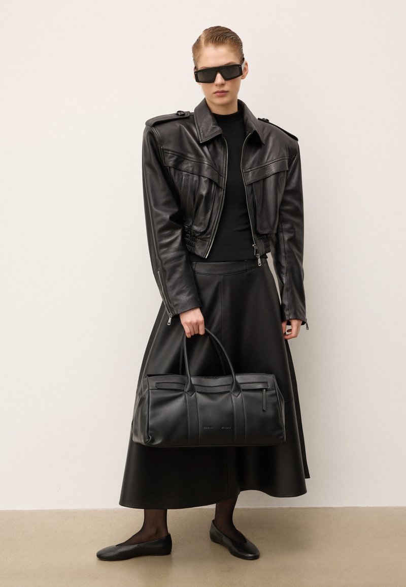 Veste en cuir noire avec épaulettes, robe noire et sac à main. Des lunettes de soleil et des ballerines noires complètent le look monochromatique.