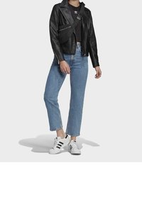 Svart läderbikerjacka över en svart kort top, i kombination med blå rakben jeans och vita sneakers med svarta ränder. Svart crossbody-väska.
