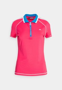 Růžové polo tričko s krátkými rukávy, vysokým límcem a zipem vpředu. Má modré a bílé akcenty podél límce a ramen.