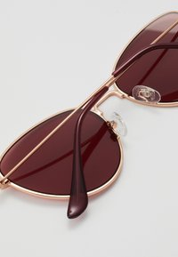 Red-tinted sunglasses with a sleek gold metal frame and thin, elegant arms. Features clear nose pads and subtle accent lines on the temples.