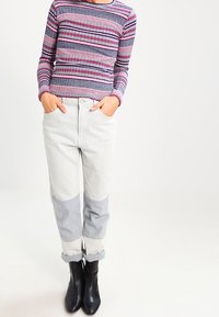 Haut à manches longues rayé rose et marine, associé à un jean patchwork gris clair. Les revers de manches retroussés et des bottines noires complètent le look.