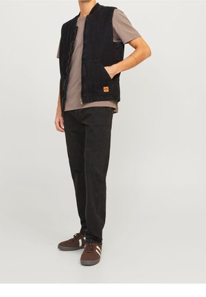 Zwarte spijkerjack met een rits, twee zijzakken en een klein oranje logopatch, gecombineerd met een grijze T-shirt en zwarte broek.