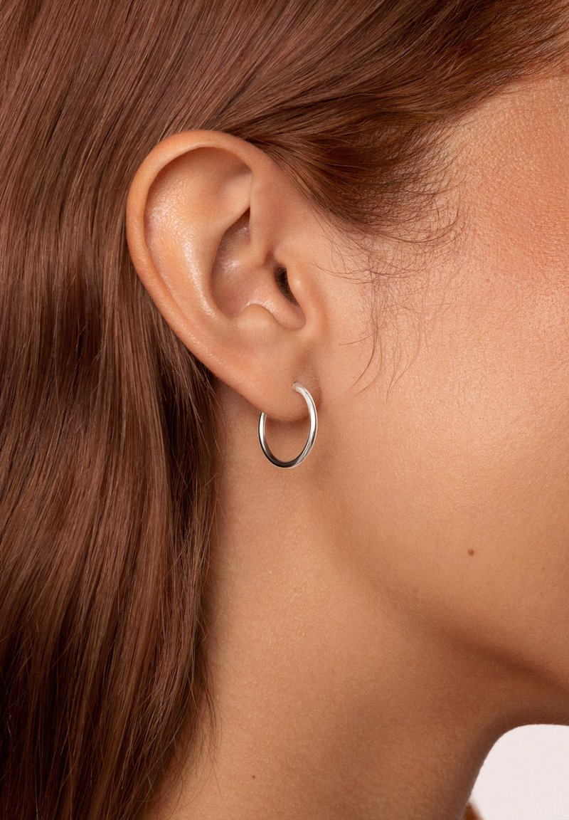 Aro de plata exhibido en la oreja, forma circular, superficie suave, ligero, con un acabado pulido y diseño minimalista.