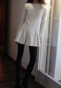 Robe en maille côtelée blanche avec ourlet évasé et manches longues, associée à des leggings noirs et des talons. Texture lisse et design minimaliste.