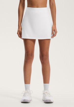 Witte, aansluitende sportrok, gladde stof met een rechte snit, midden boven de dijen, gecombineerd met witte sneakers en sokken.