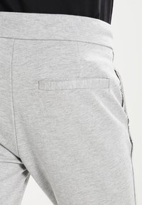 Pantalones de chándal grises con una textura suave, con una cintura elástica y un bolsillo trasero. La tela parece ligeramente jaspeada.