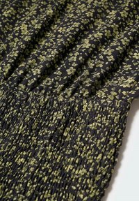 Black fabric with scattered green floral print, featuring gathered and smocked texture for stretch and fit. Detailed with fine, small flowers.