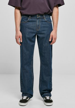 Dark blue denim jeans with a straight leg cut, five-pocket design, and a button waist closure. Worn with black sneakers.