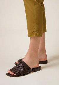Bruine leren instapsandalen met textuur, ribbelige banden en een lage blokhak, gecombineerd met mosterdkleurige cropped broek.