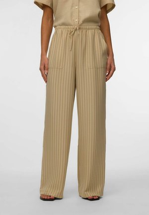 Pantalon beige à jambes larges avec fines rayures verticales noires, taille élastique avec cordon de serrage, poches latérales, porté avec des sandales noires ouvertes.