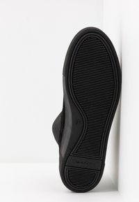 Suela de goma negra con un diseño texturizado que presenta surcos horizontales y verticales. Parte superior de ante con una forma elegante y redondeada. Logo de la marca visible.
