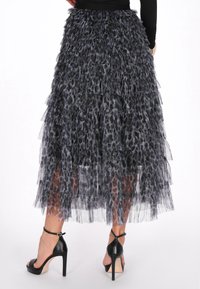 Sort og grå lagdelt tulle midi-nederdel med dyreprint, båret med sort langærmet top og sorte højhælede ankel-sandaler med rem.