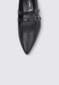 Zapato de tacón negro de piel con punta afilada, dos tiras decorativas con hebillas, textura suave, diseño minimalista y plantilla acolchada.