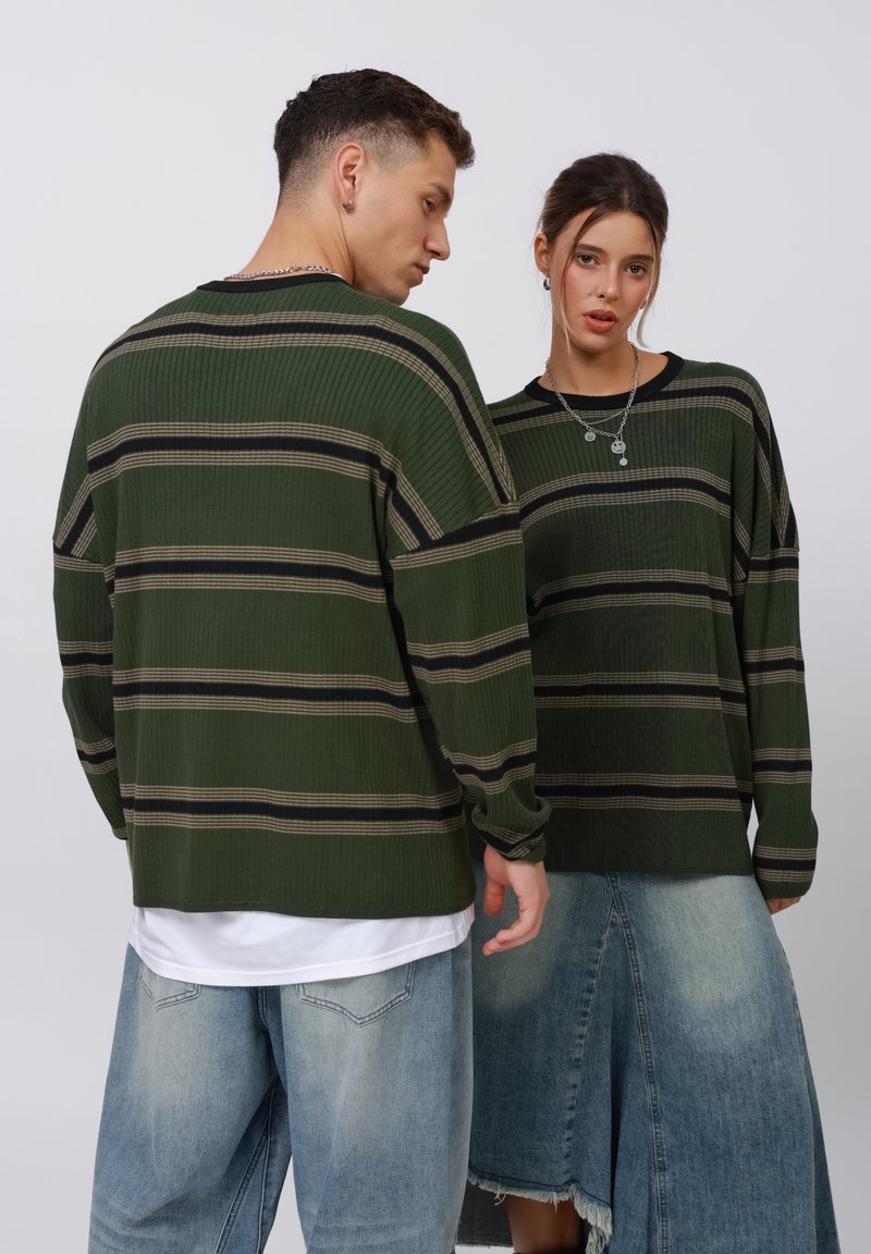 Grün gestreifte Langarmshirts mit gerippter Textur, die schwarze und beige Streifen aufweisen. Getragen mit hellblauen Baggy-Jeans und einem Jeansrock.