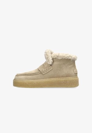 Botte en daim beige avec un col en fourrure blanche duveteuse, doté une sangle à boucle et une semelle en caoutchouc épaisse et texturée.