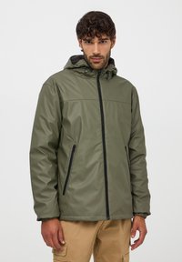 Giacca impermeabile verde oliva con cappuccio, zip frontale e due tasche laterali. Texture liscia e polsini regolabili per una vestibilità aderente.