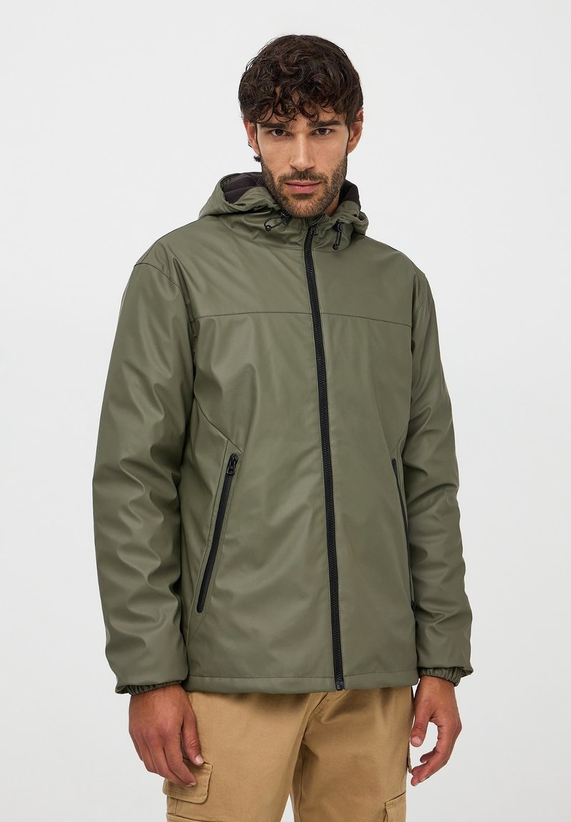 Giacca impermeabile verde oliva con cappuccio, zip frontale e due tasche laterali. Texture liscia e polsini regolabili per una vestibilità aderente.