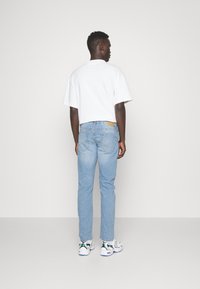 White short-sleeve t-shirt paired with light blue denim jeans, featuring a tan leather patch on the back and white sneakers with green accents.