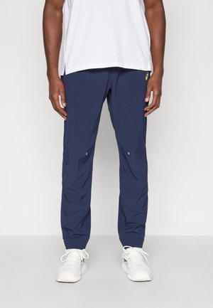 Mørkeblå træningsbukser i letvægtsstof, med elastiske manchetter, lynlåslommer og et side-logo på bæltet.