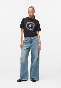 Black cotton t-shirt with a circular white graphic design, paired with light blue, wide-leg distressed denim jeans, featuring ripped accents.