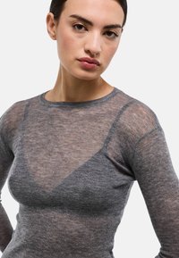 Haut à manches longues gris transparent avec texture côtelée, présentant un design en forme de V au niveau de l'encolure et de subtiles paillettes partout.