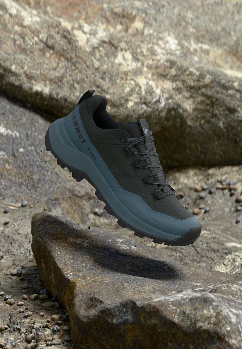 Mustas ja sinises värvitoonis Mammuti matkajalats tugevdatud tallaga, ripub künklikul alal väikeste kivide ja suurte kividena.