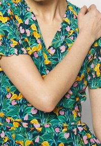 Robe portefeuille florale avec un fond teal, des motifs de fleurs roses vives et jaunes, des manches courtes et un décolleté en V.
