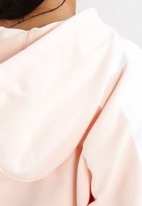 Sudadera de color rosa claro con una textura suave, que presenta una capucha tradicional y una franja blanca en contraste a lo largo de un hombro.