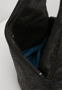 Musta nahkainen laukku, jossa on teksturoitu ulkopinta ja turkoosi kangasvuori sisällä, esittäen vetoketjullisen aukon ja sisätilojen yksityiskohtia.