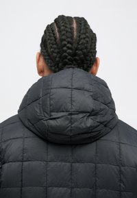 Black quilted puffer jacket with a large hood. Features a smooth texture and grid pattern visible on the fabric. Designed for warmth.