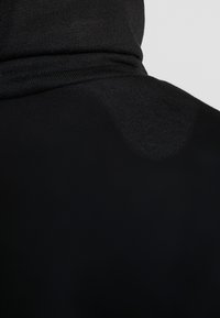 Felpa nera con cappuccio caratterizzata da un alto colletto e una texture a coste. Il tessuto è liscio con una leggera lucentezza in alcune aree, mostrando sottili variazioni di tonalità.