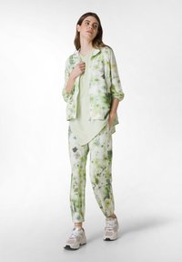 Chándal ligero con estampado floral verde, que incluye una chaqueta con cremallera y pantalones ajustados. Presenta una parte superior en capas y zapatillas blancas.