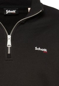 Pulóver negro con cremallera hecho de tejido texturizado. Presenta una cremallera plateada y un logo "Schott" blanco con acento rojo. Diseño de alto cuello.