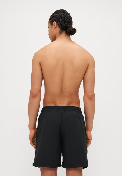Shorts de bain noirs en tissu léger, dotés d'une taille élastique et d'une poche arrière unique. Présentés de dos.