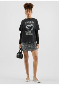 Zwarte grafische T-shirt met een discobalontwerp, gecombineerd met een sprankelende zilveren paillettenshort en zilveren flats. Zwarte handtas accentueert de look.