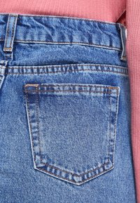 Světle modré džíny z denimu s jednou zadní kapsou s oranžovým šitím, texturovanou tkaninou a mírně vybledlým vzhledem.