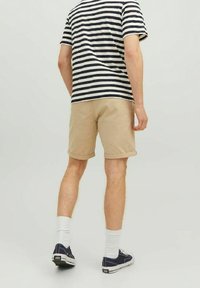 Beżowe szorty z podwiniętymi nogawkami, w parze z granatową bluzką w białe paski. Model nosi białe skarpetki i granatowe trampki.