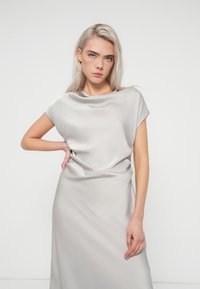 Robe en satin gris clair avec un décolleté drapé et des manches courtes, présentant un détail de nœud à la taille et une texture lisse.