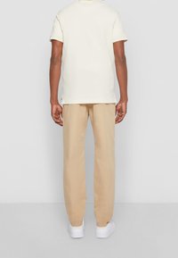 Beige bomullbyxor och en krämfärgad t-shirt. T-shirten har rak passform och sidokilar. Båda plaggen har en avslappnad passform och bärs med vita sneakers.