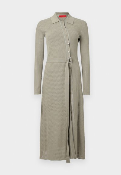 Robe longue côtelée en kaki doux. Comprend un col avec boutons sur le devant et une ceinture en tissu avec une boucle argentée. Manches longues.