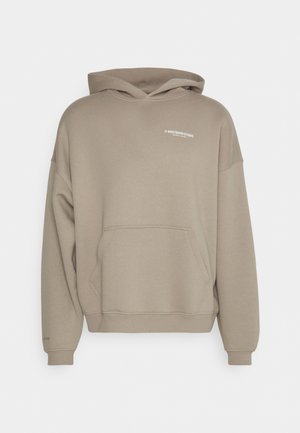 Sweat à capuche beige avec poche kangourou à l'avant et petit texte de logo blanc sur la partie supérieure gauche de la poitrine et au poignet gauche.