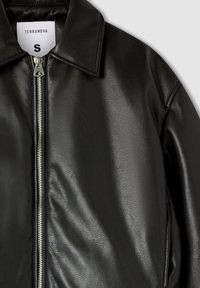 Giacca nera in pelle sintetica con zip argentata, colletto a punta e etichetta bianca che mostra la marca e la taglia piccola.