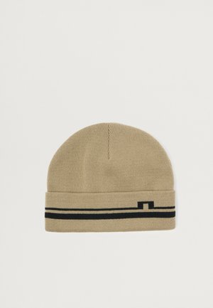 Touca de malha bege com punho dobrado, apresentando uma faixa preta e um pequeno detalhe gráfico. Textura suave e ajustada.