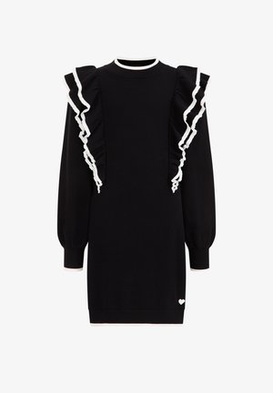 Robe noire à manches longues avec des volants bordés de blanc le long des épaules et un petit cœur blanc près de l'ourlet.