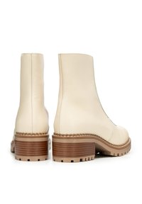 Botas de tobillo de cuero crema con una textura suave, punta redonda y tacón grueso marrón. La suela presenta un patrón de tracción resistente.
