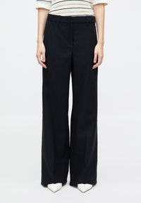 Navy wide-leg trousers in a smooth fabric with a high waistband. The model is wearing white pointed-toe shoes.