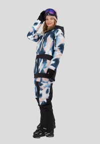 Kolorowy zestaw narciarski z niebieskim, różowym i czarnym abstrakcyjnym wzorem, z zamkiem błyskawicznym w kurtce i spodniami w stylu cargo. Zawiera rękawice i gogle.