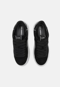 Svarta mockaskor med en vit gummisula, utrustade med tjocka svarta snören och en minimalistisk design, märkta med "KARL LAGERFELD" på tungan.